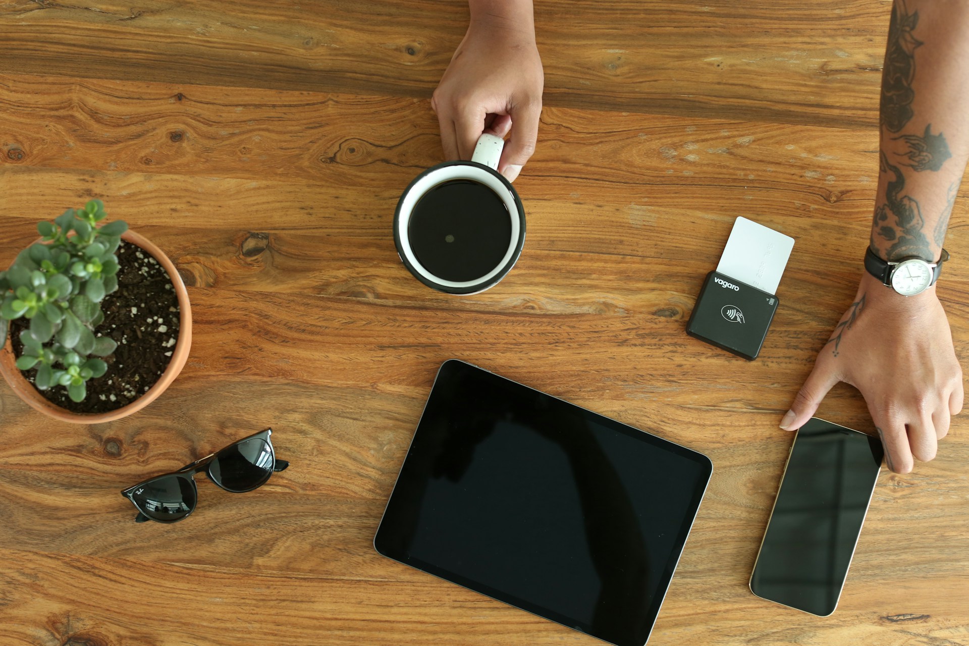 Hands, coffee, and technology on a wooden table.