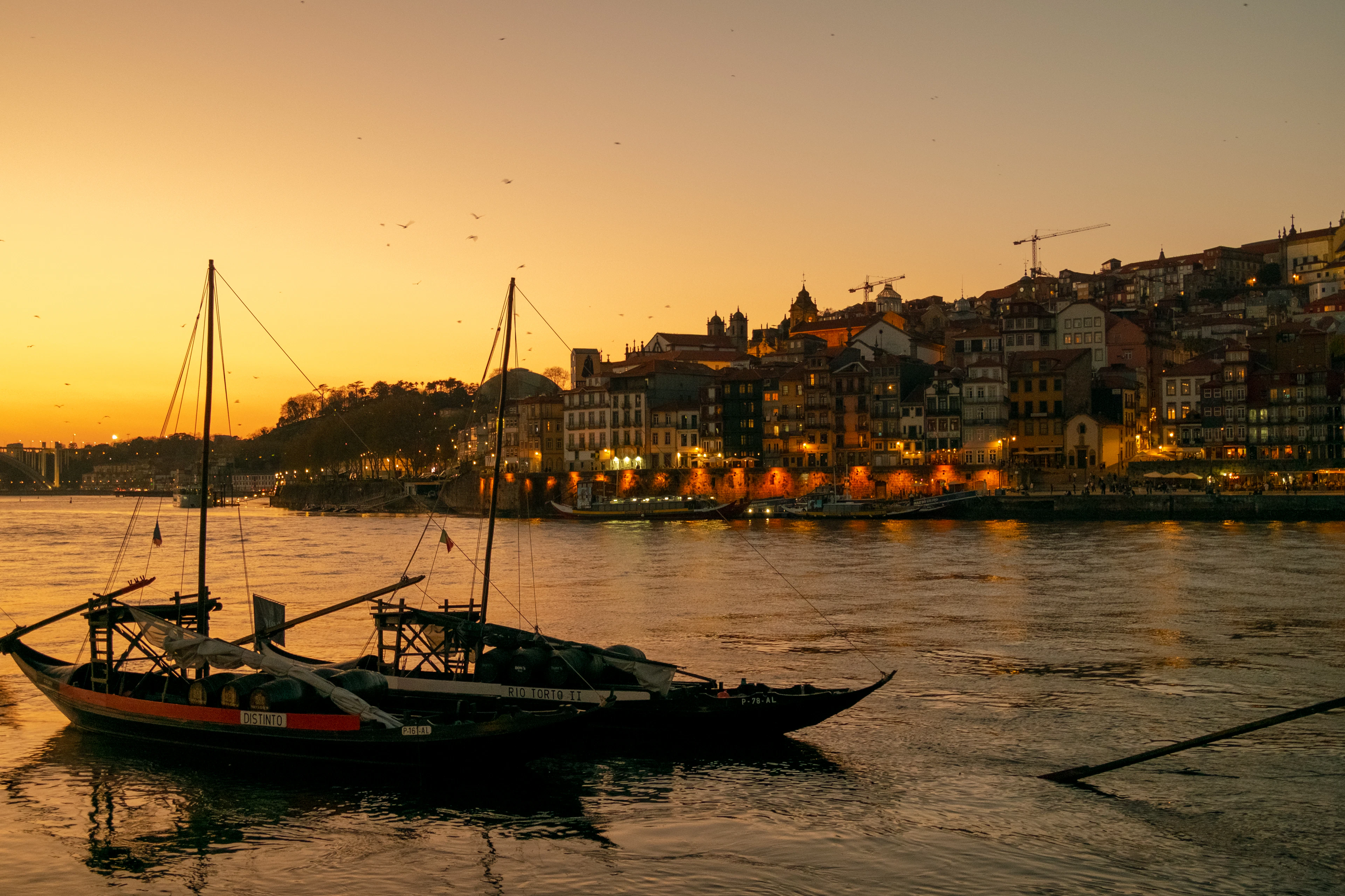 Traditional boats rest on the Douro at sunset with Porto's illuminated hillside skyline behind.