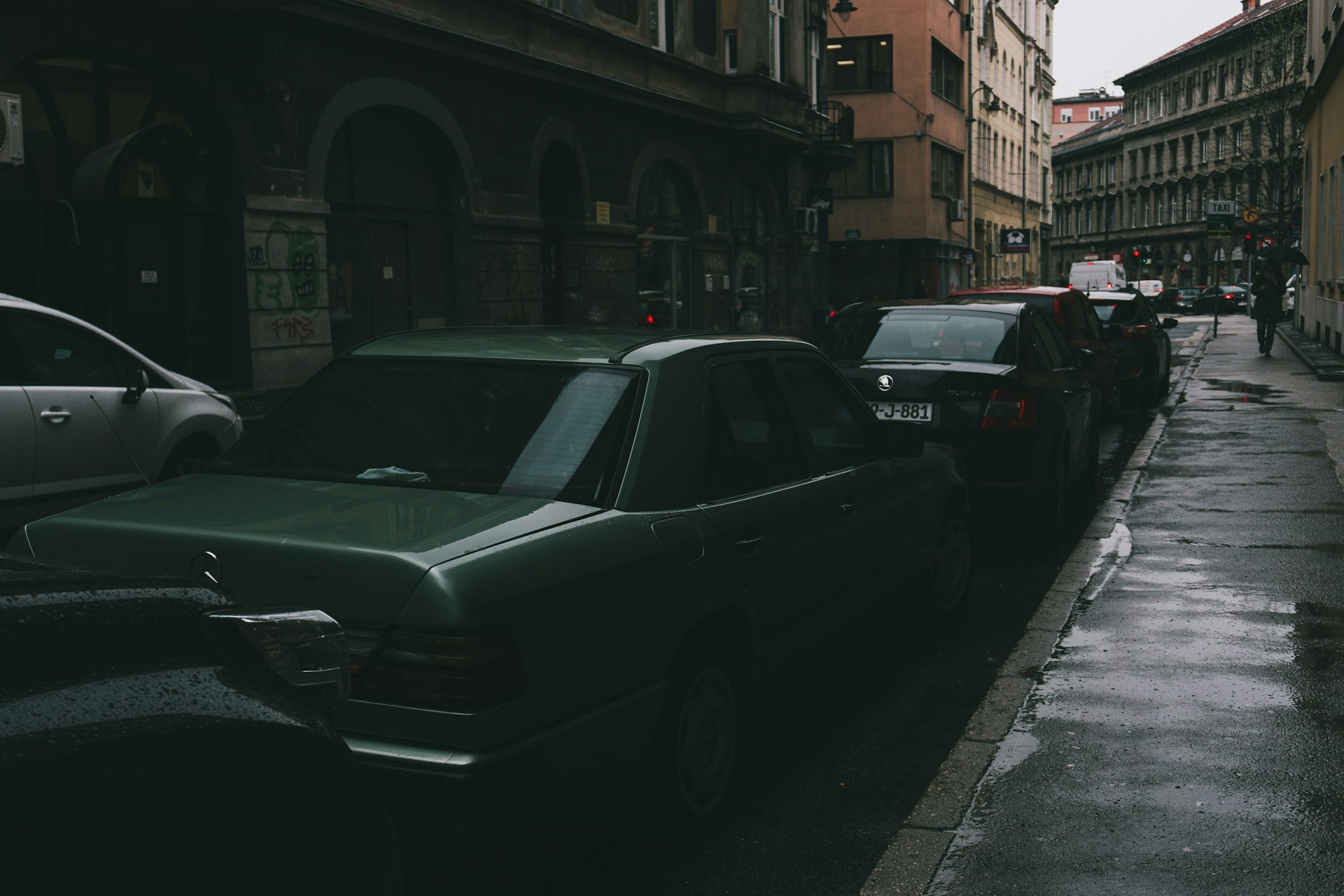 Cars parked on a narrow, wet city street.