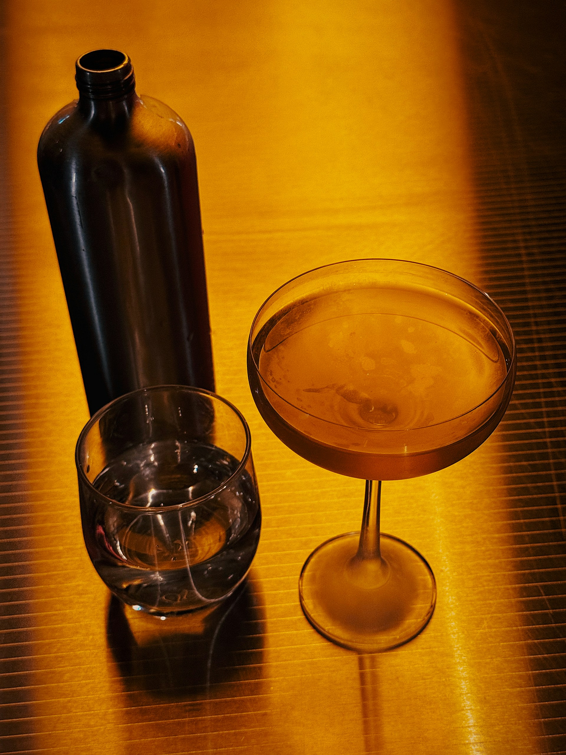 A bottle, water, and cocktails on a golden surface.
