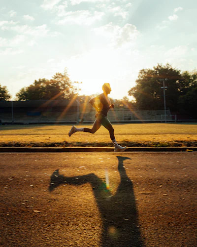 Corredor en plena zancada sobre una pista de atletismo, iluminado por la luz dorada del atardecer