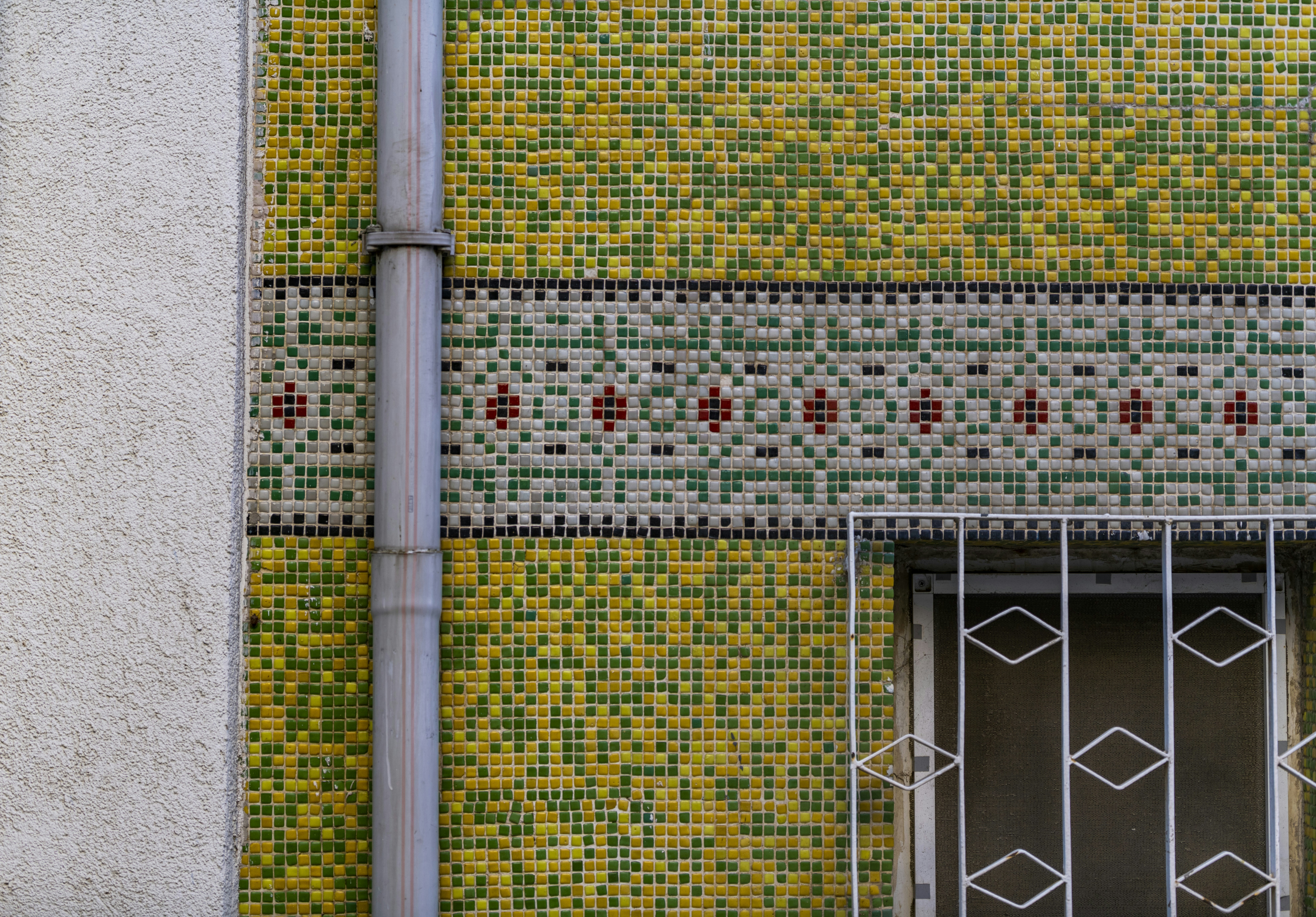 Wall with colorful tiles, drainpipe, and window.
