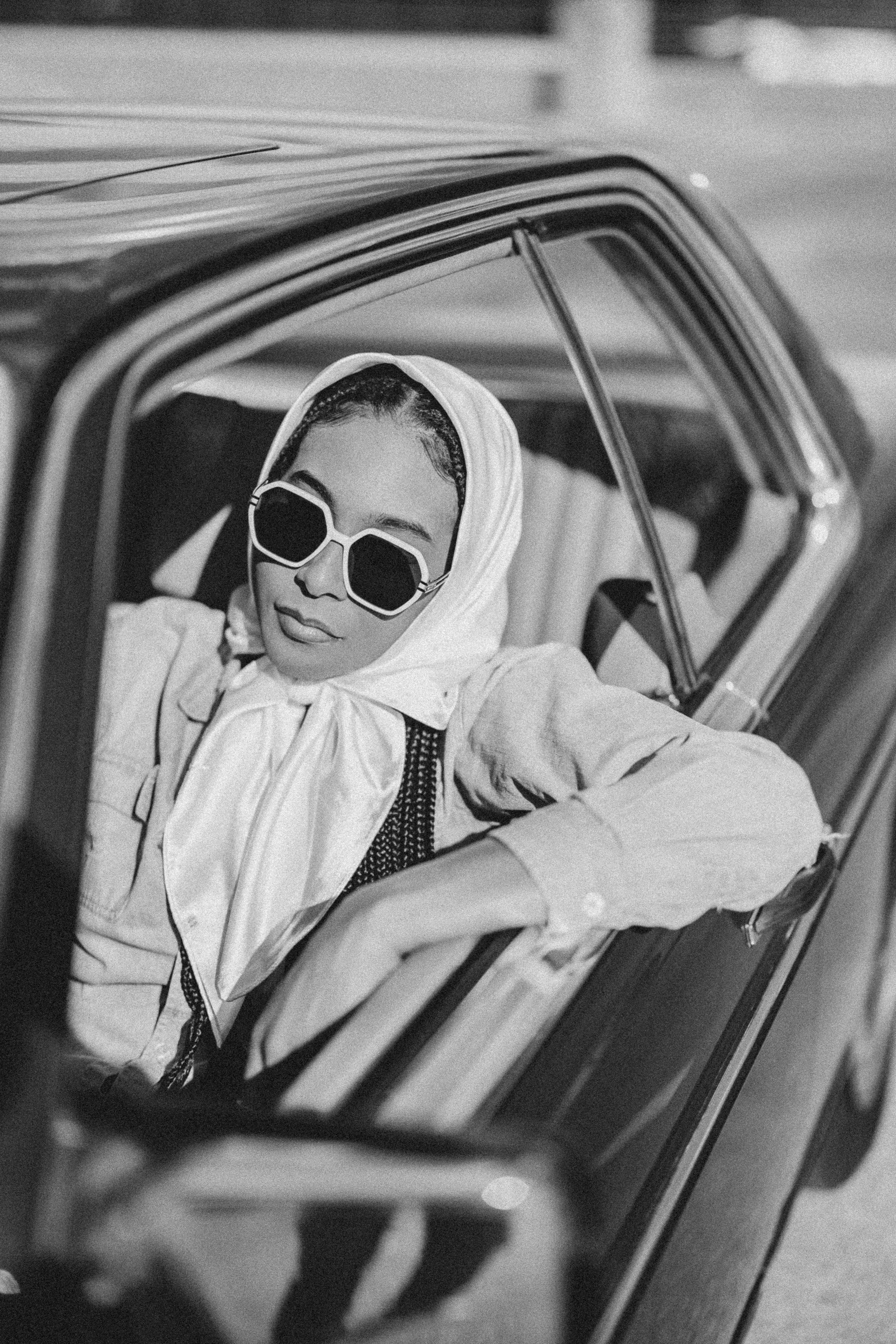 Woman poses in a vintage car, wearing sunglasses.