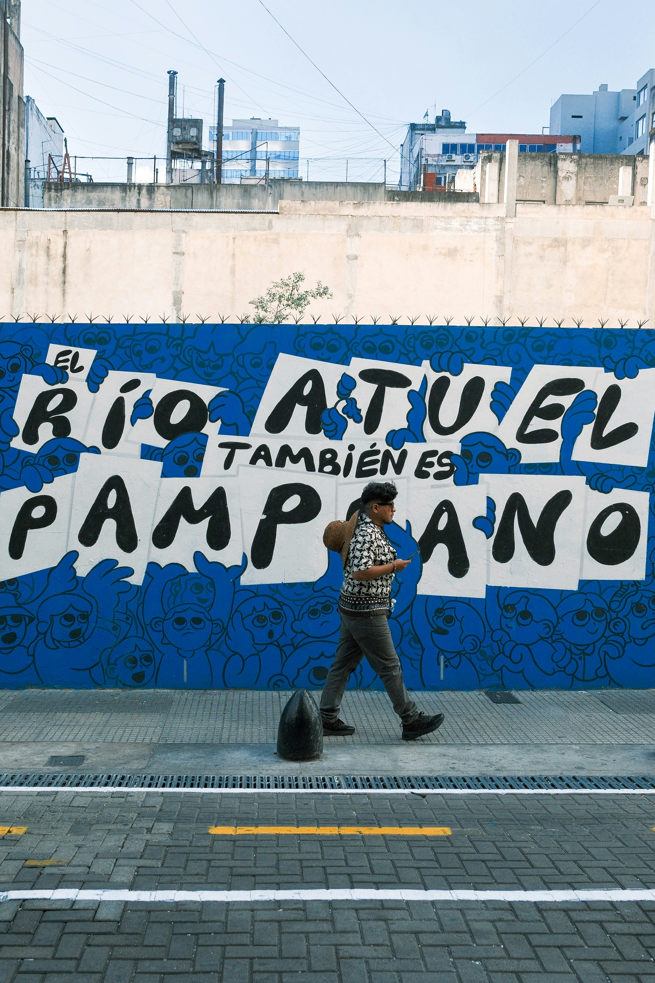 Homem passa por um mural azul vibrante.