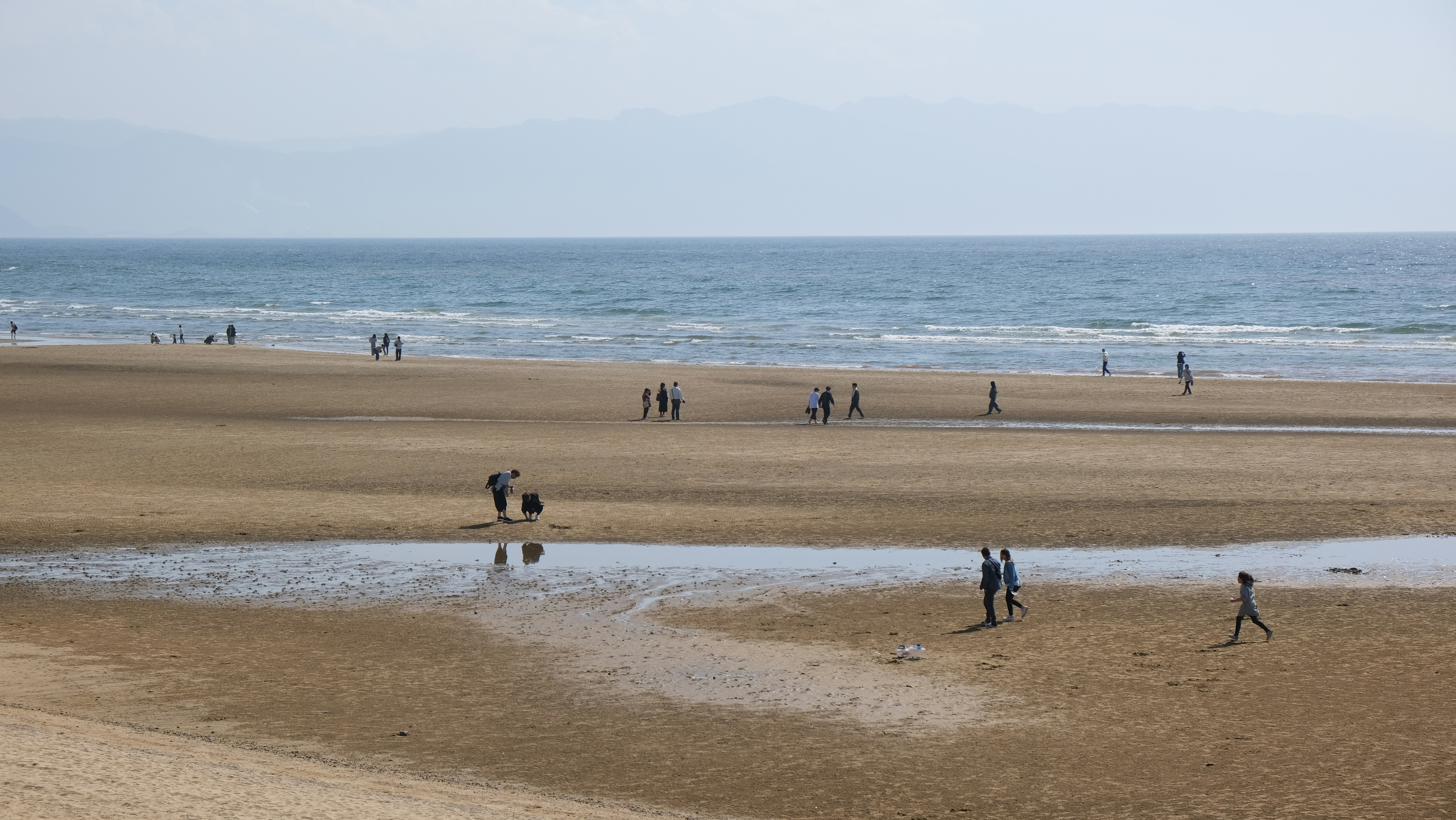 People are walking on a sandy beach.