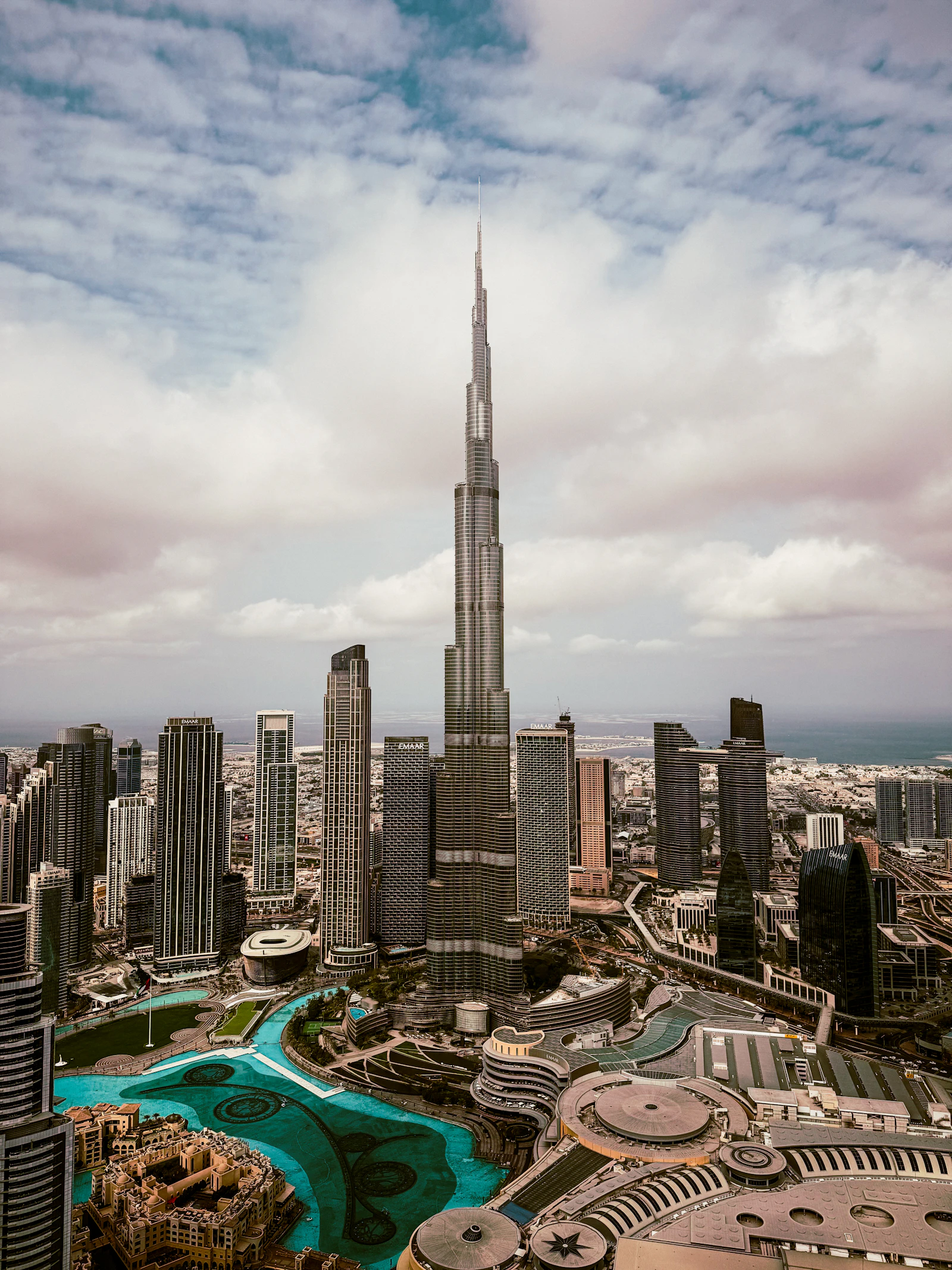 Aerial view of Downtown Dubai centered on the Burj Khalifa, with the Burj Lake and the curved roofline of The Dubai Mall below