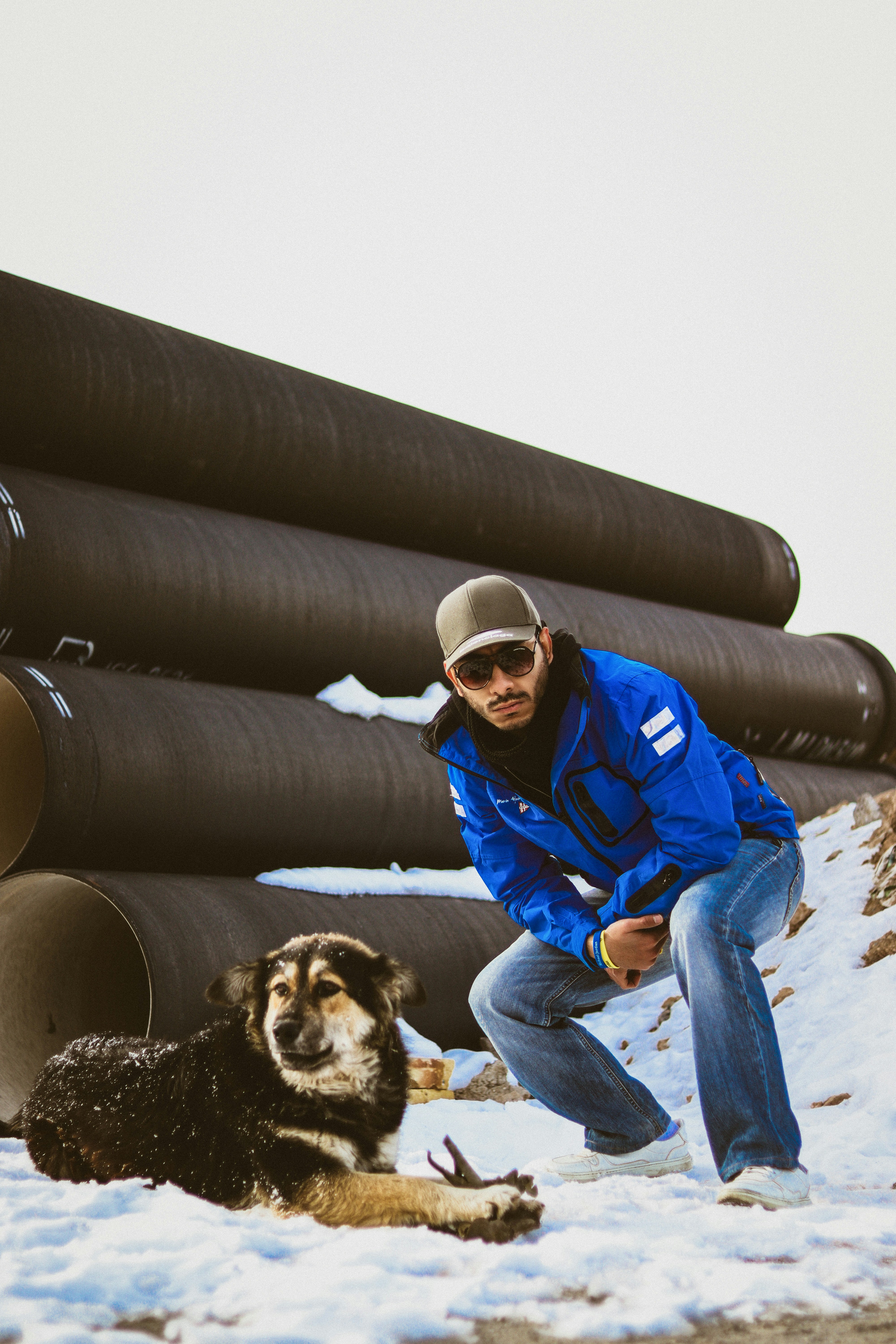 Man poses with his dog in front of large pipes.
