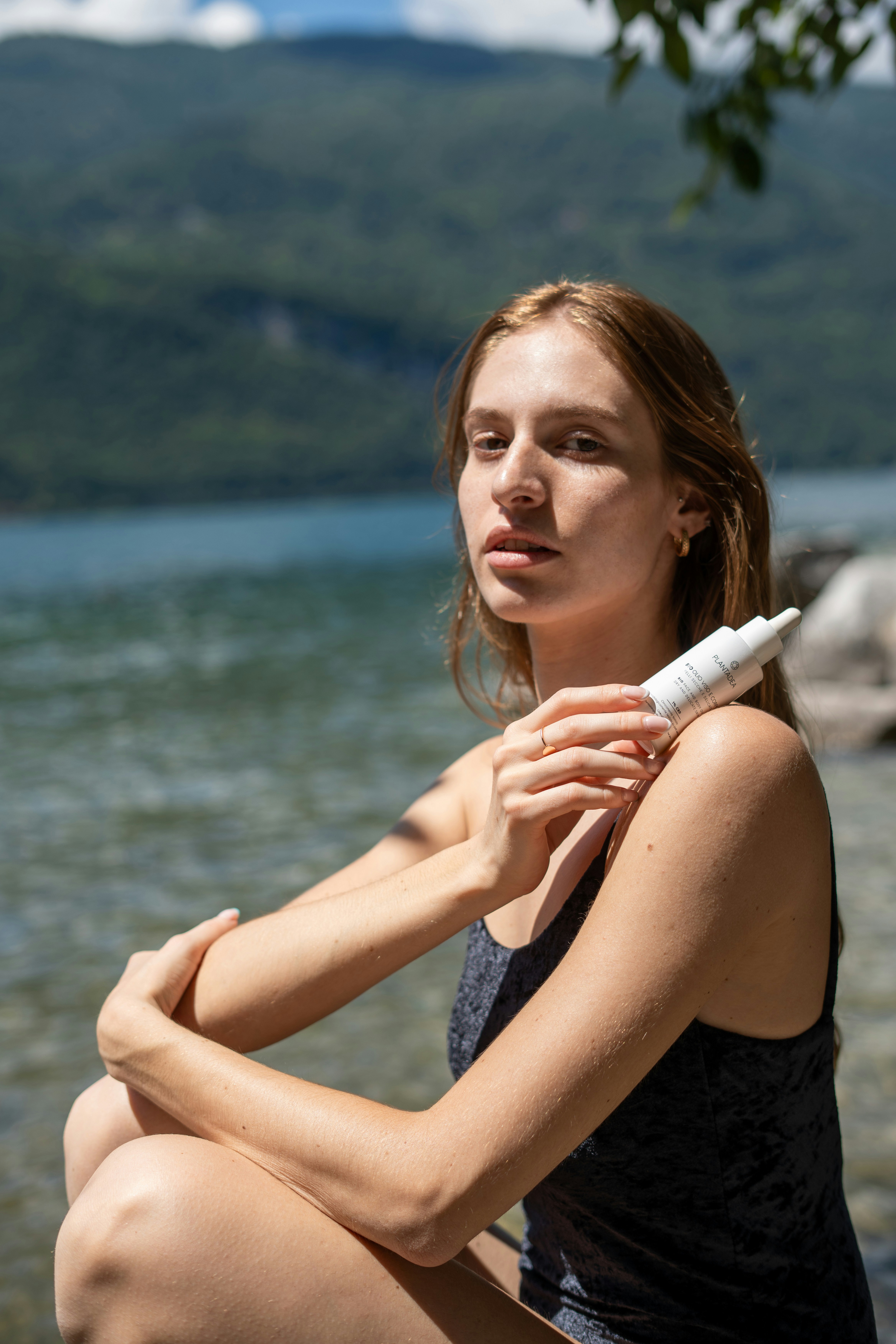 Woman holding skincare product near the water