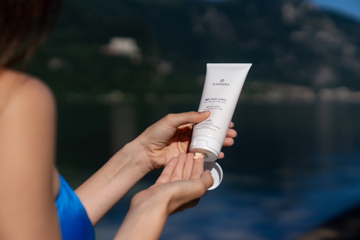 A woman applying lotion from a tube while outdoors in daylight