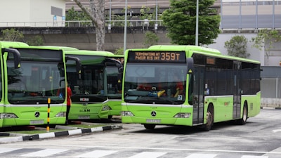 Green buses are parked at a bus depot.