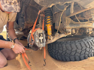 Man secures vehicle's undercarriage with straps.