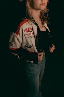 A woman poses, wearing a bomber jacket.