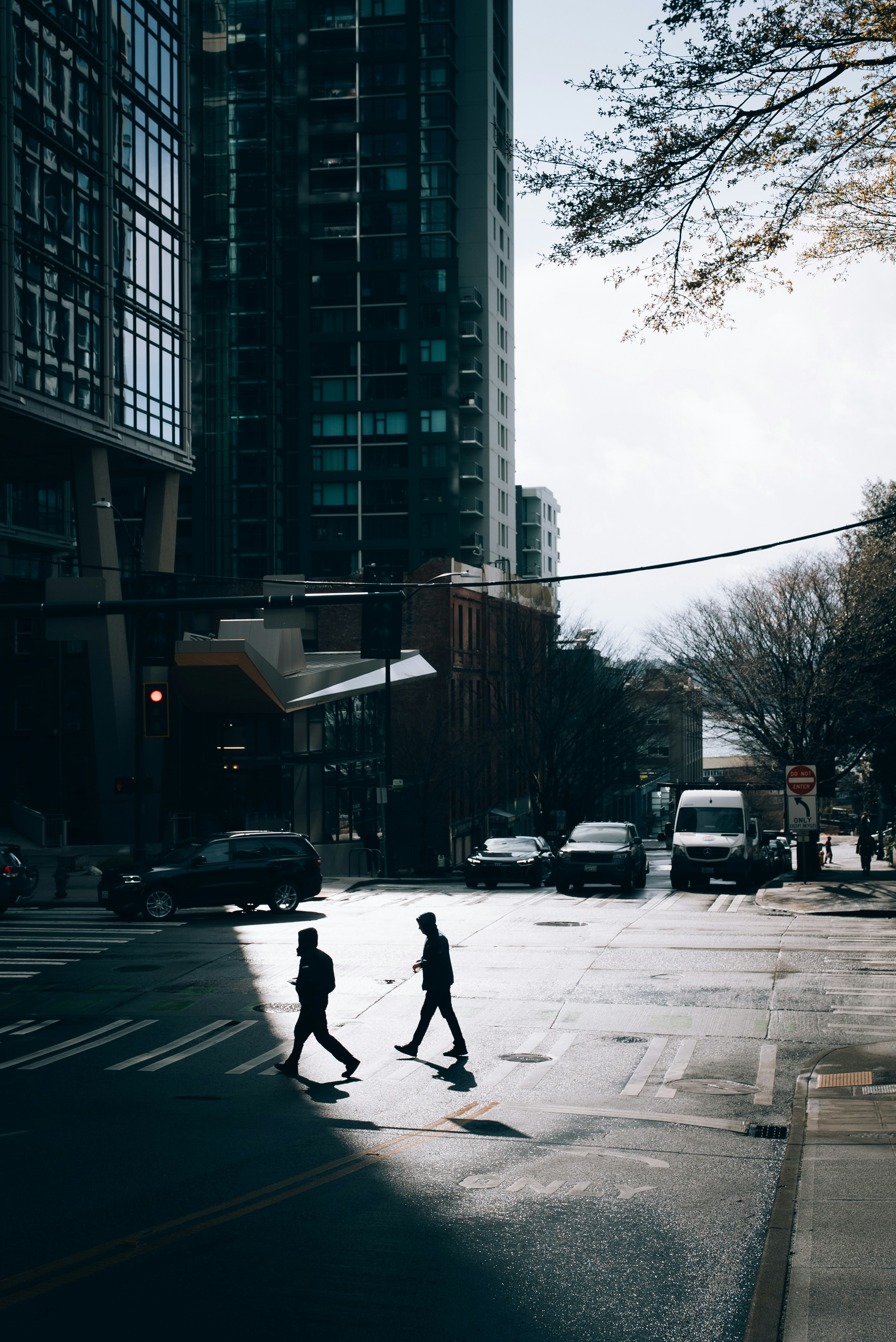 People cross a city street in the shadow.