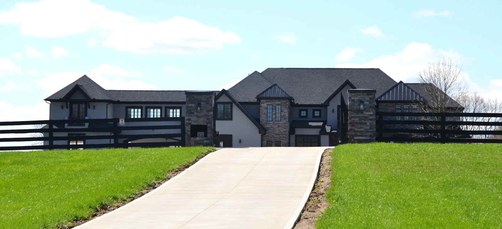 A dark-trimmed modern house behind a ranch fence.