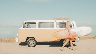 Surfer with surfboard walks toward a beach van.