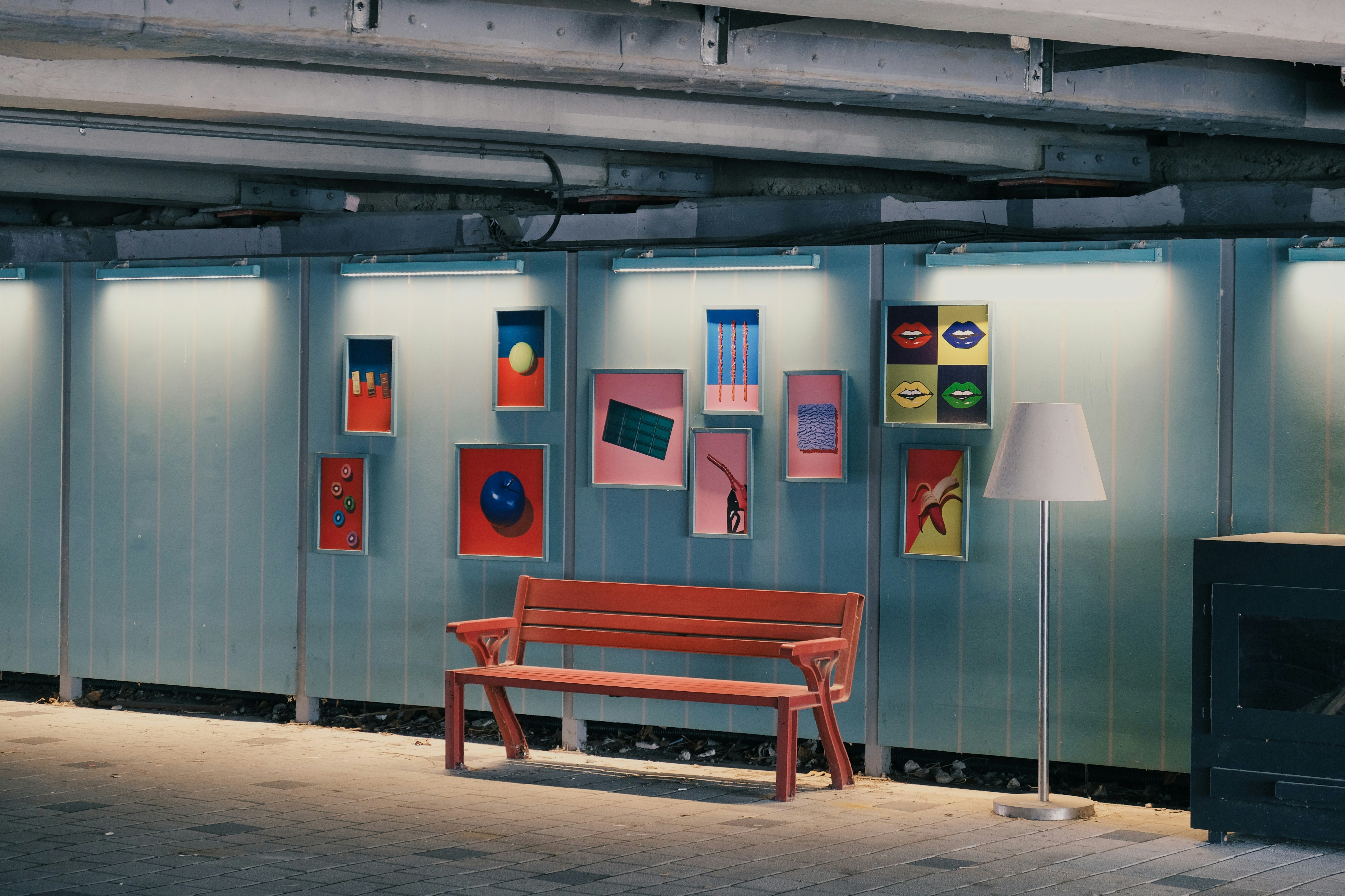 Art is displayed near a bench in an underground passage.