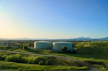 Two water tanks sit on a hill under the sky.