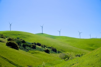 Wind turbines stand atop rolling green hills.