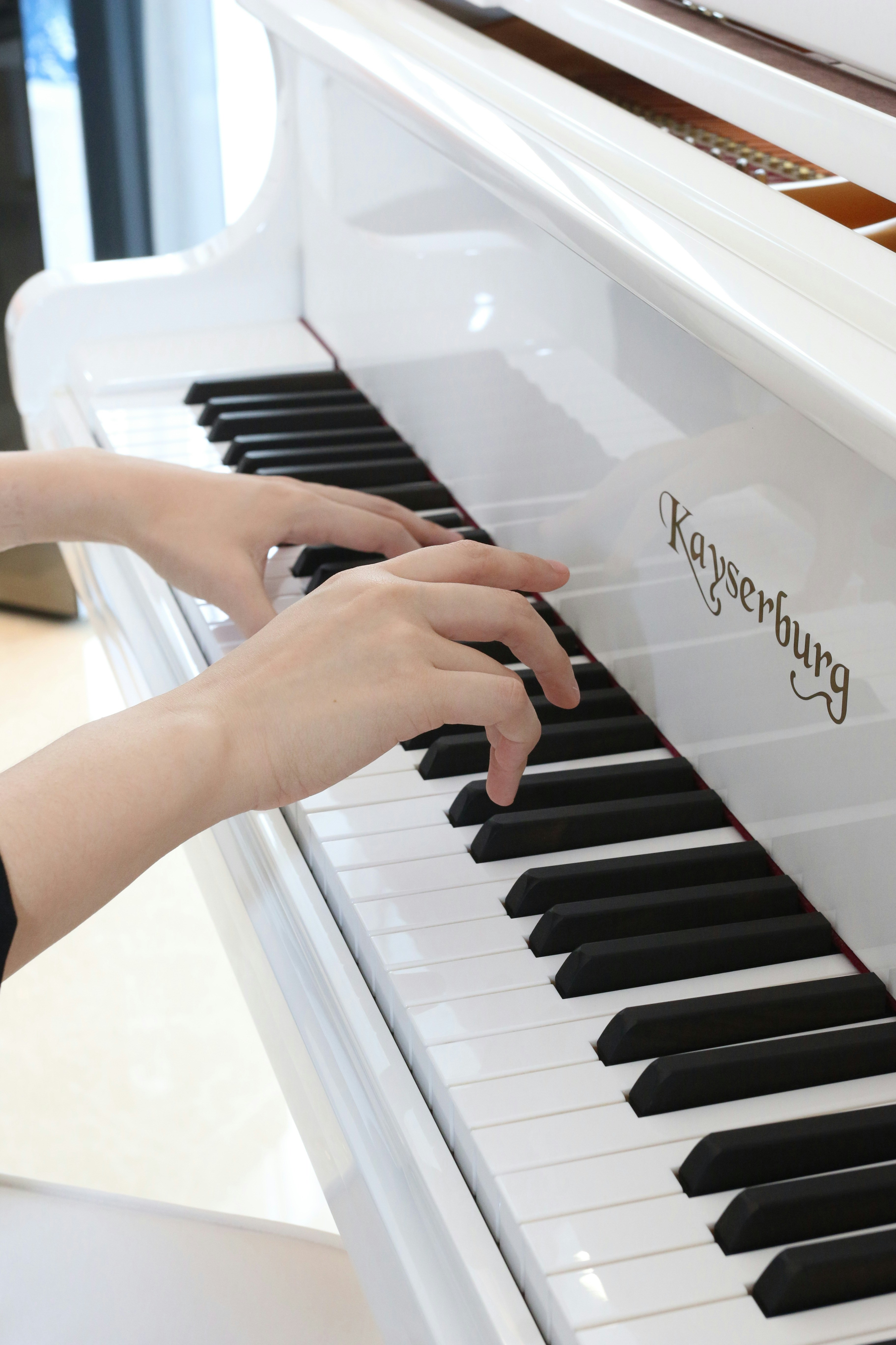 Hands are playing the keys of a white piano.