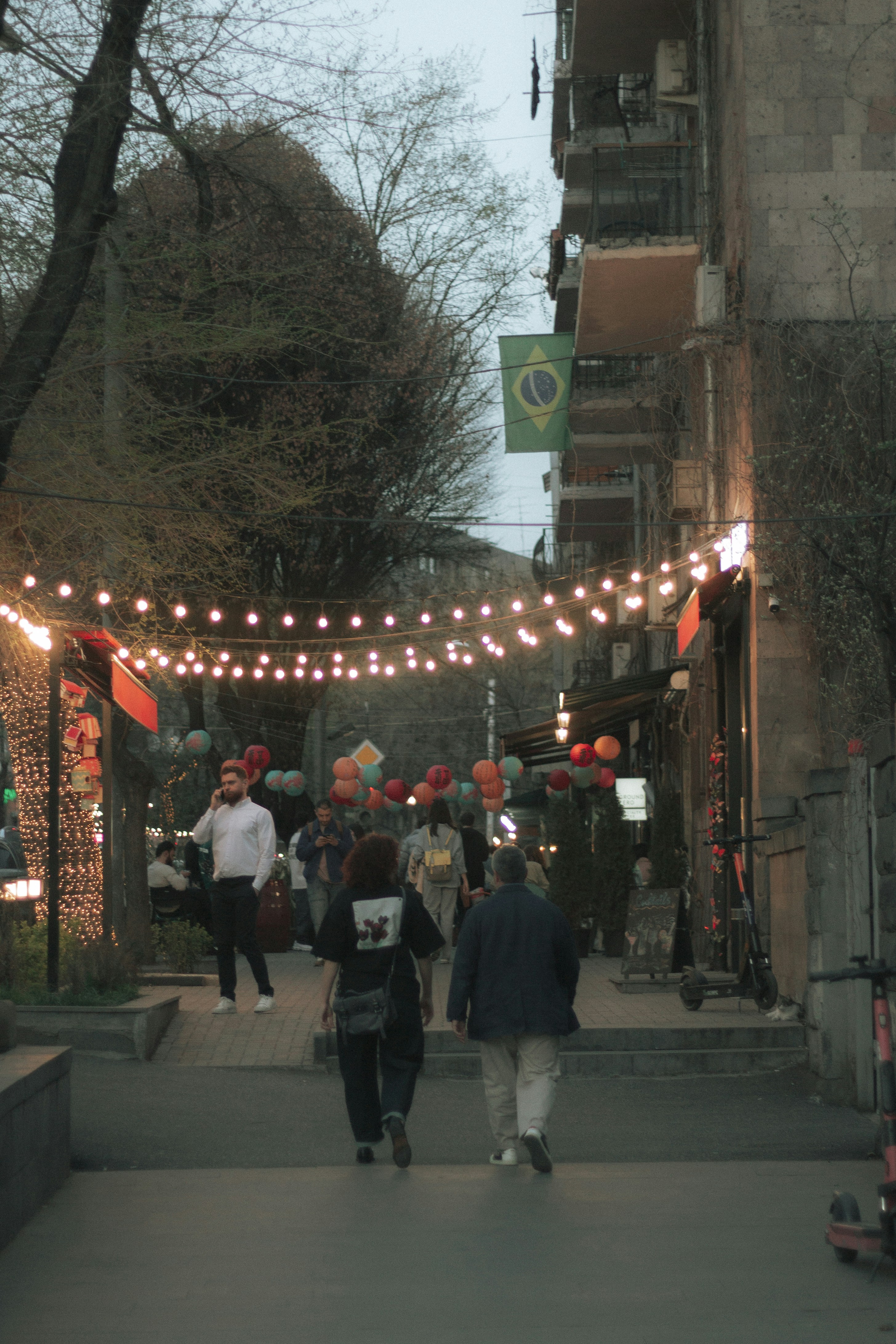 People stroll under street lights and a brazilian flag.