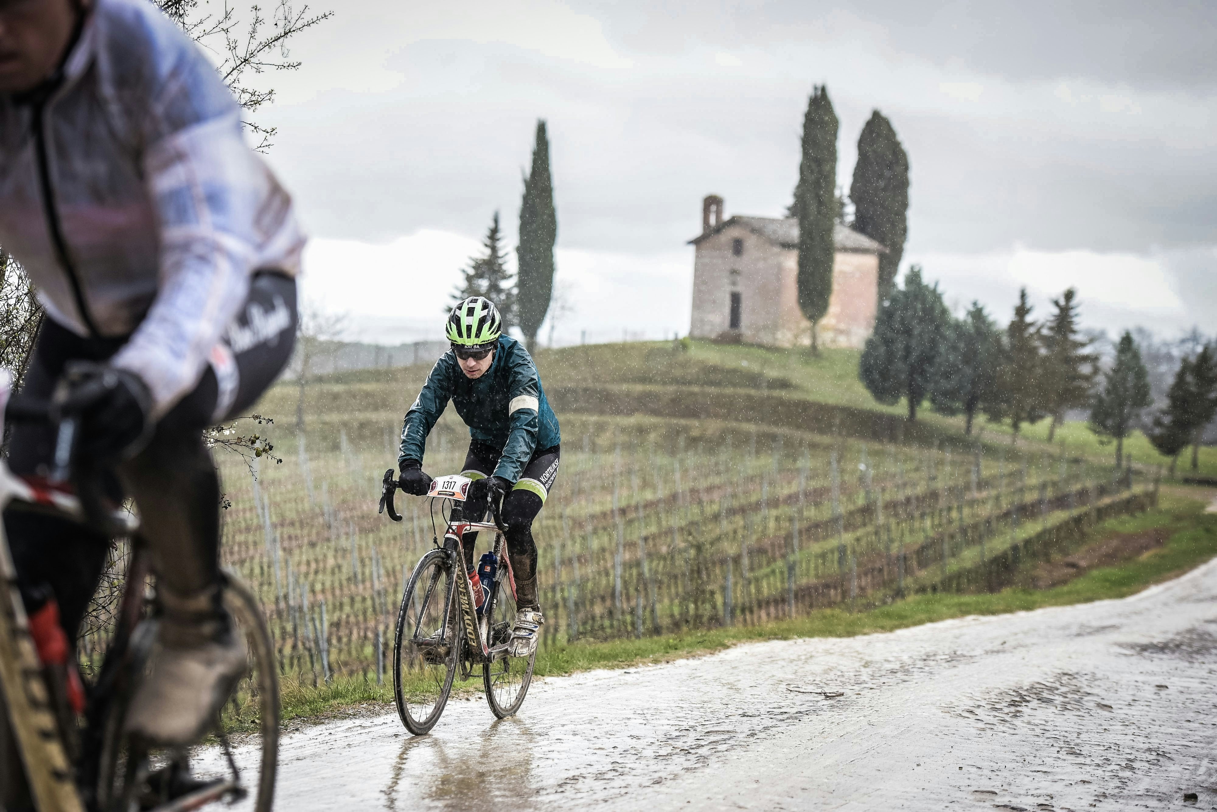 Cyclists ride their bikes on a wet, rural road.