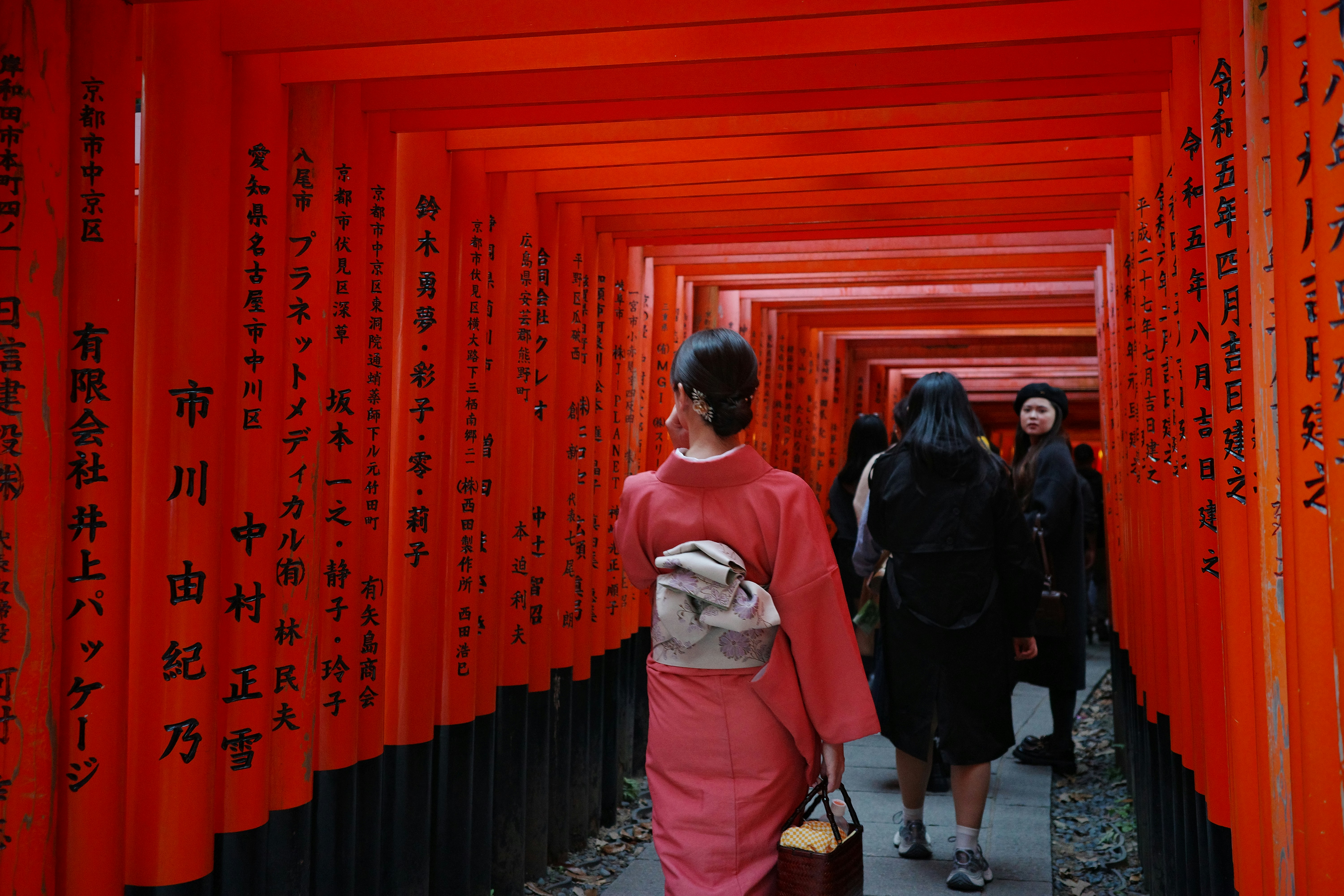 People walk through a red torii gate tunnel.
