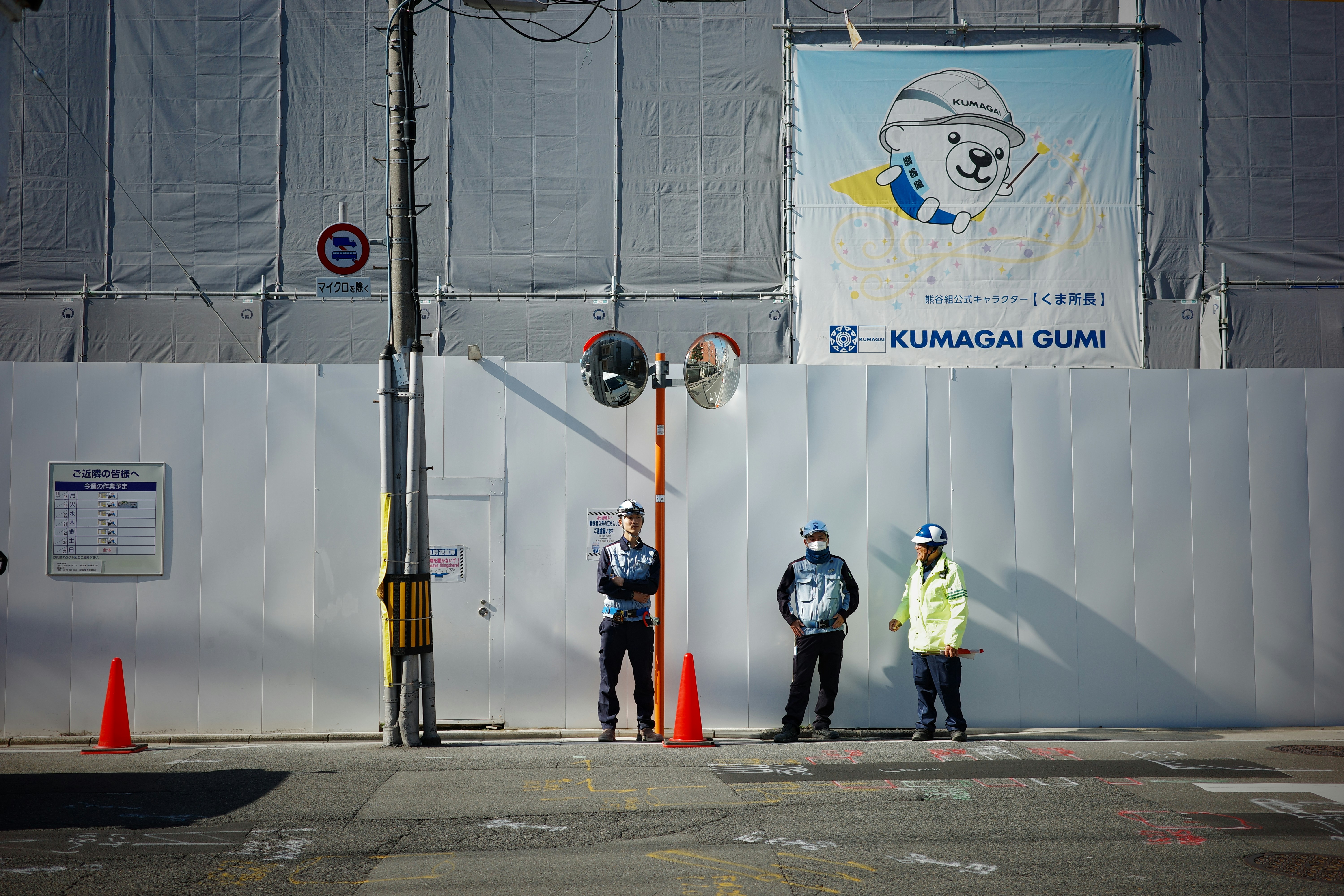 Construction workers standing near a wall with a sign.