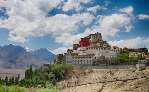 A monastery sits atop a cliff in the mountains.
