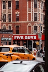 A busy street scene with a five guys restaurant.