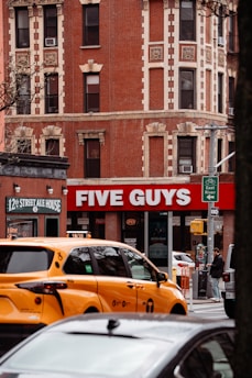 A busy street scene with a five guys restaurant.