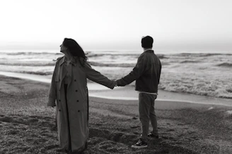 Couple holds hands on a beach, looking at the ocean.
