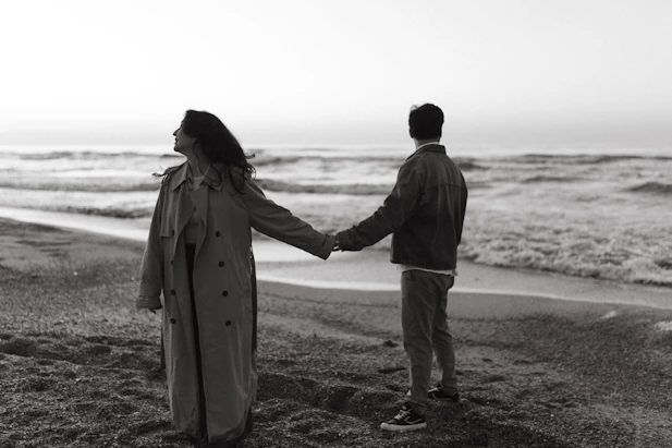 Couple holds hands on a beach, looking at the ocean.