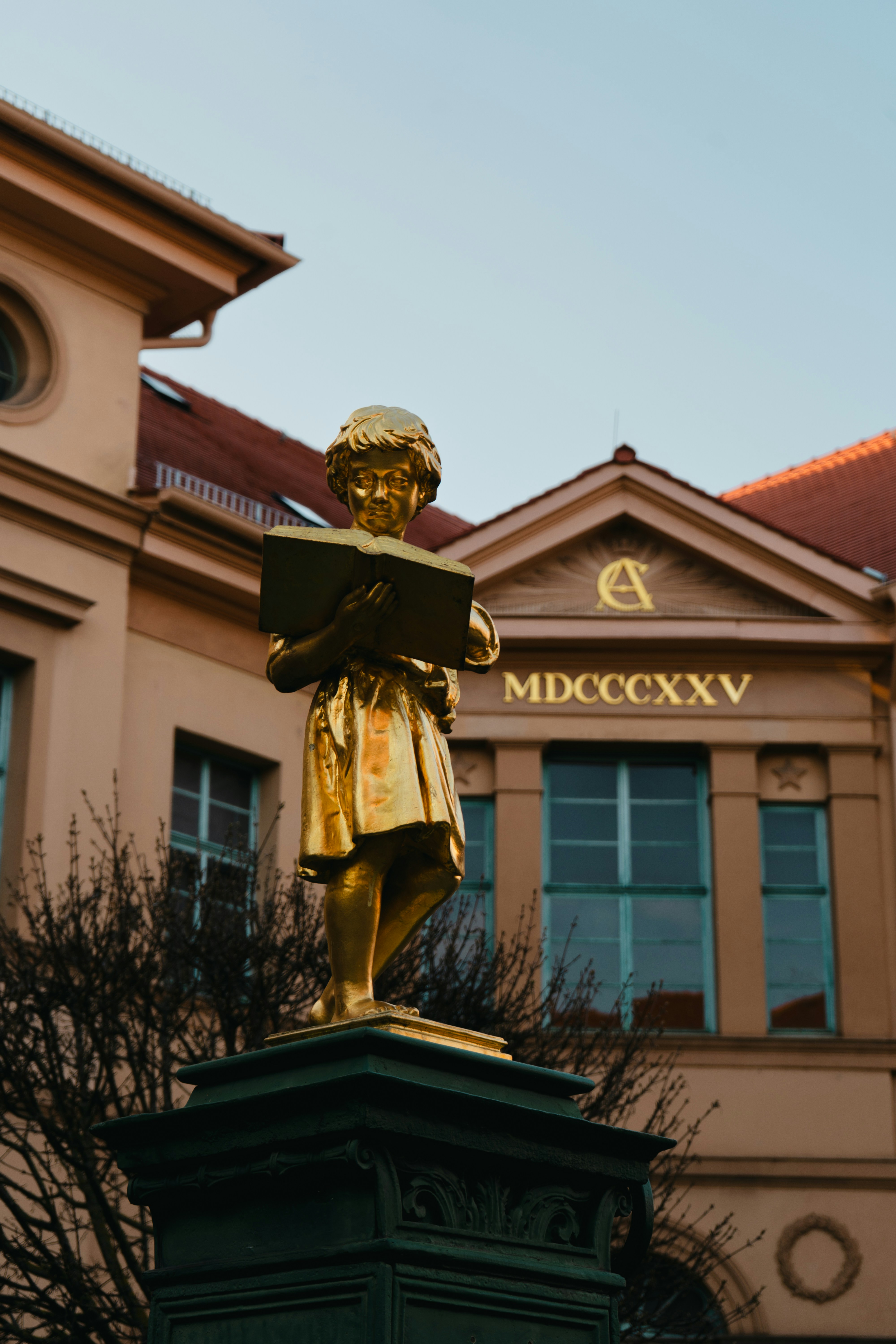 A golden statue of a girl reading a book.
