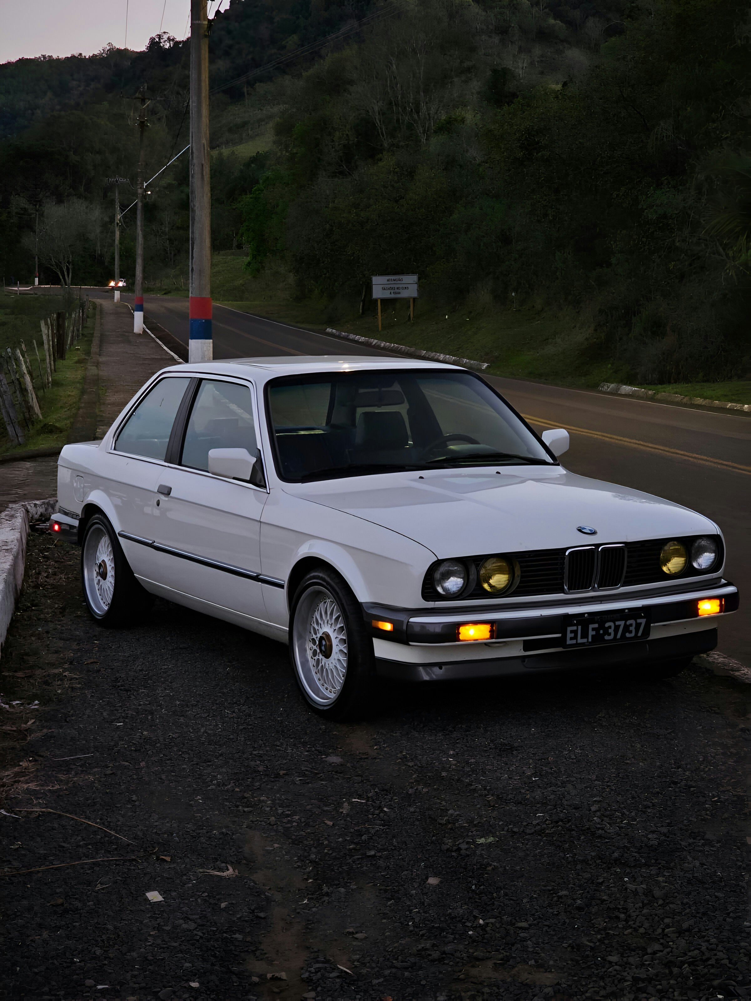 A white BMW car is parked on a road