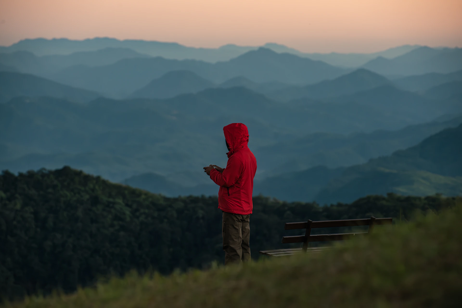 Person in red hoodie looks at phone by the mountains.