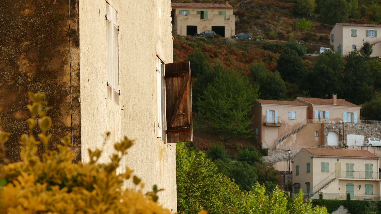 An open wooden shutter on a stone building above a hillside of rooftops