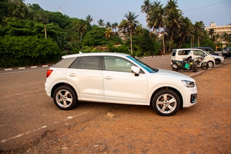 A white suv is parked in front of trees.