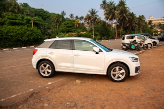 A white suv is parked in front of trees.