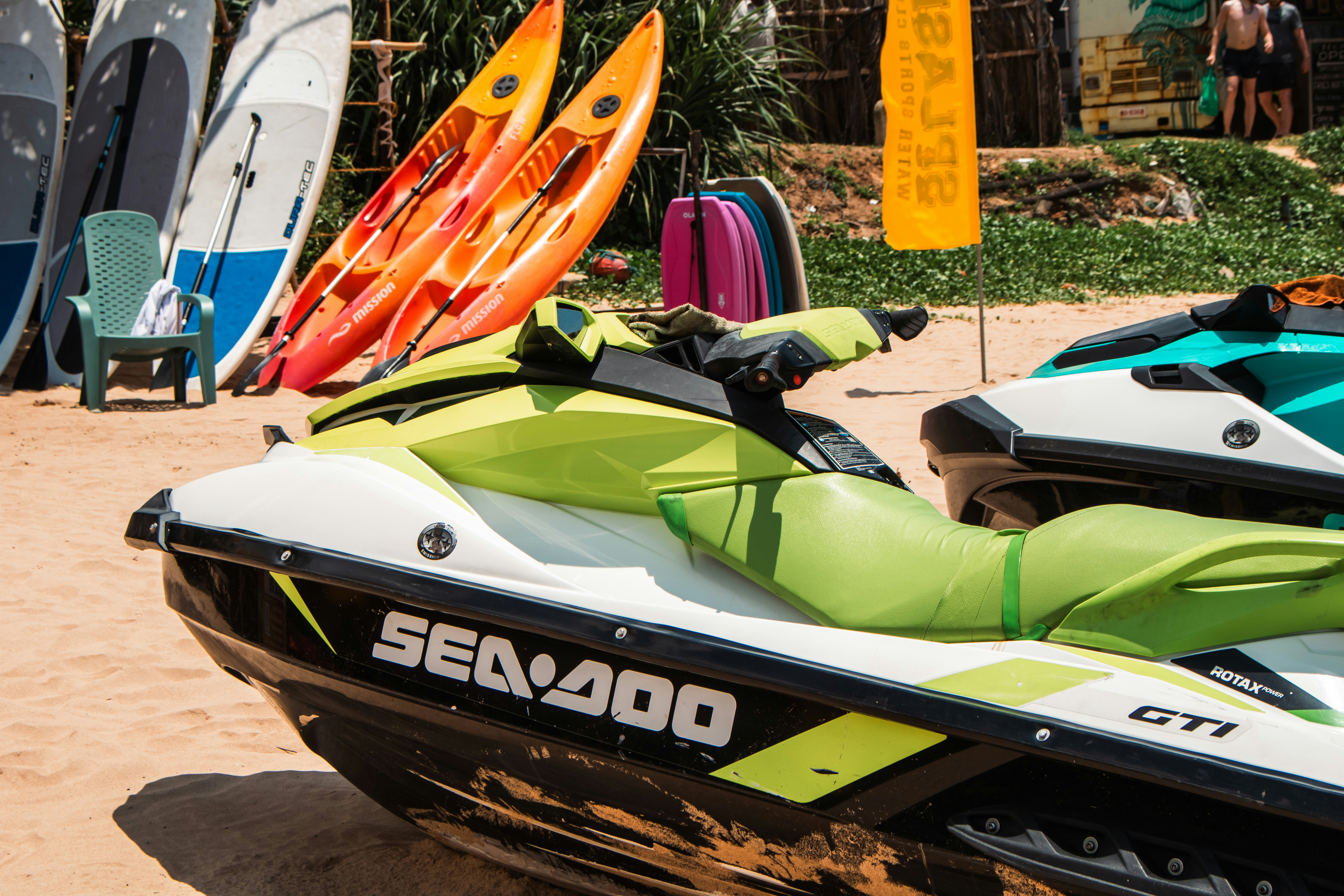 Jet skis and kayaks sit on a sandy beach.
