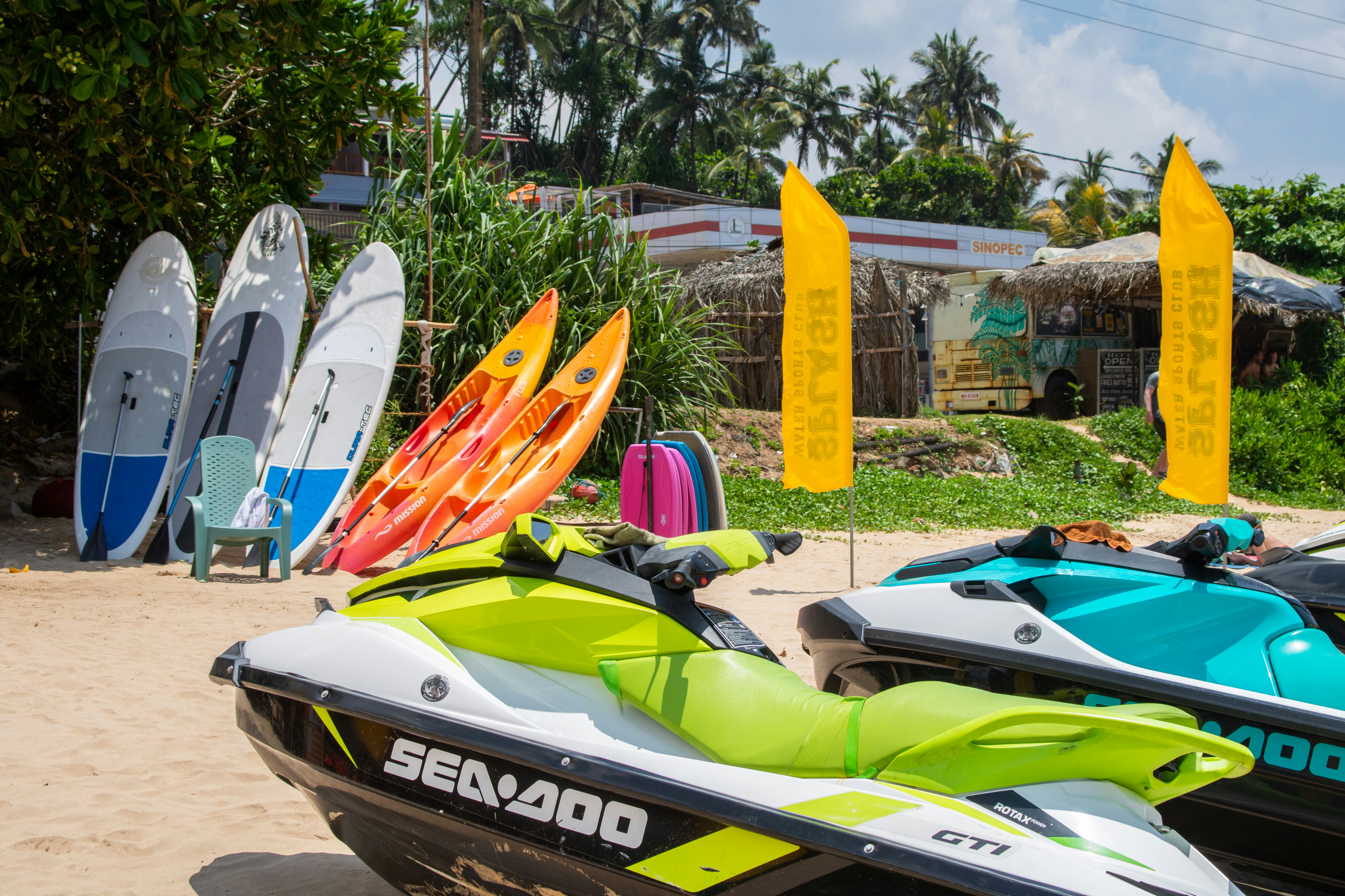 Several colorful Sea-Doo jet skis (PWCs) are parked on the sunny, sandy beach of Mirissa ready for use.