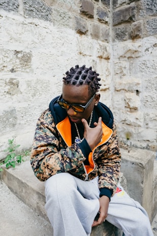 A stylish man poses against a stone wall.
