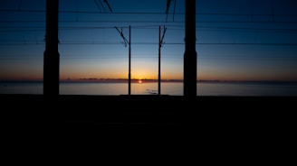 Sunrise over water framed by electrical poles.