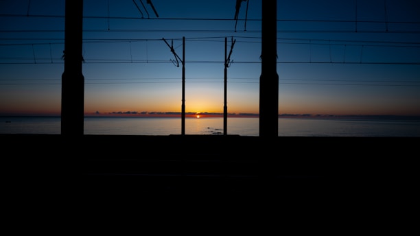 Sunrise over water framed by electrical poles.