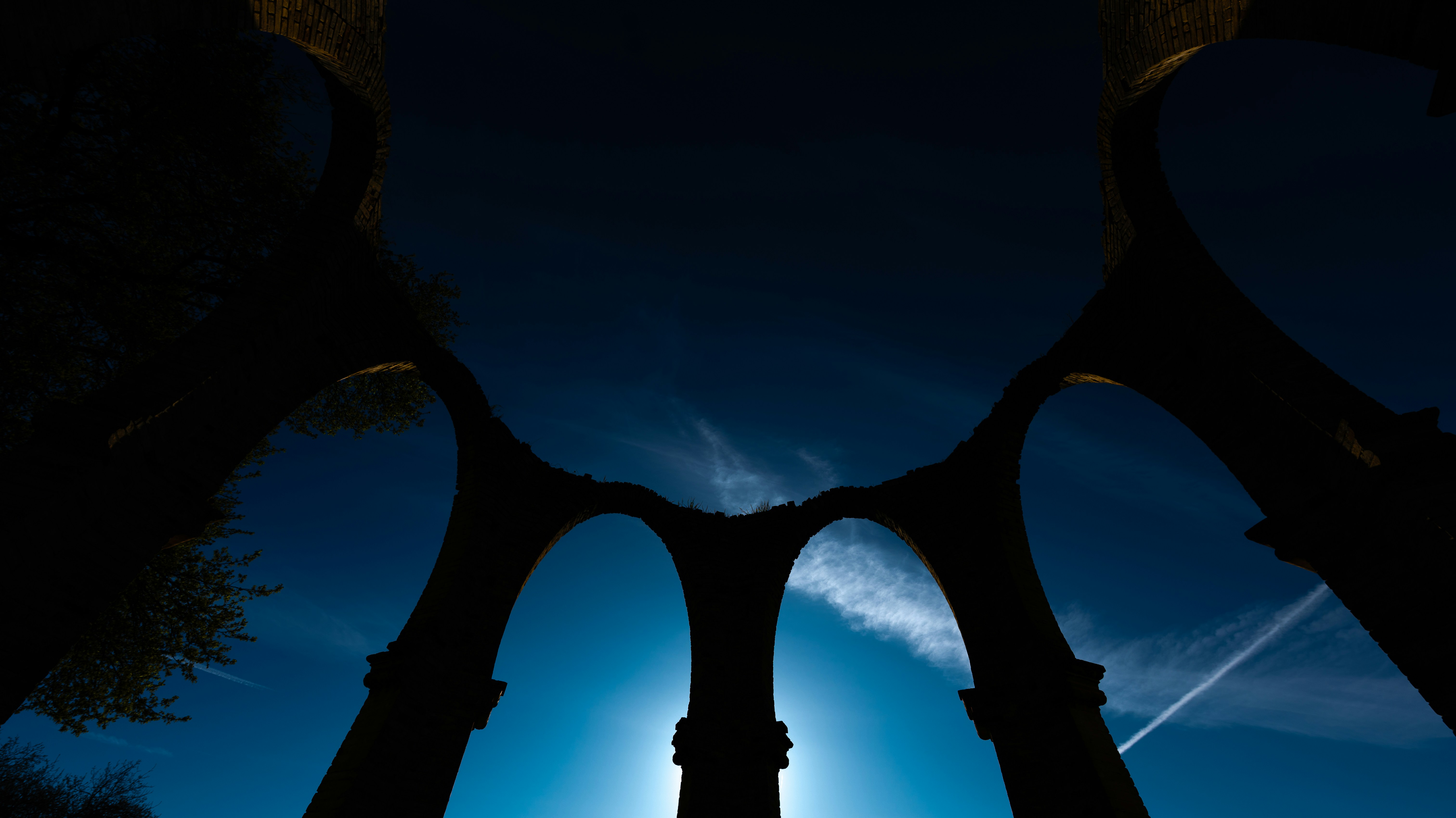 La luce del sole filtra attraverso antichi archi di pietra su un cielo azzurro.