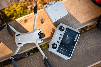 Drone, controller, and battery charger on a wooden bench.