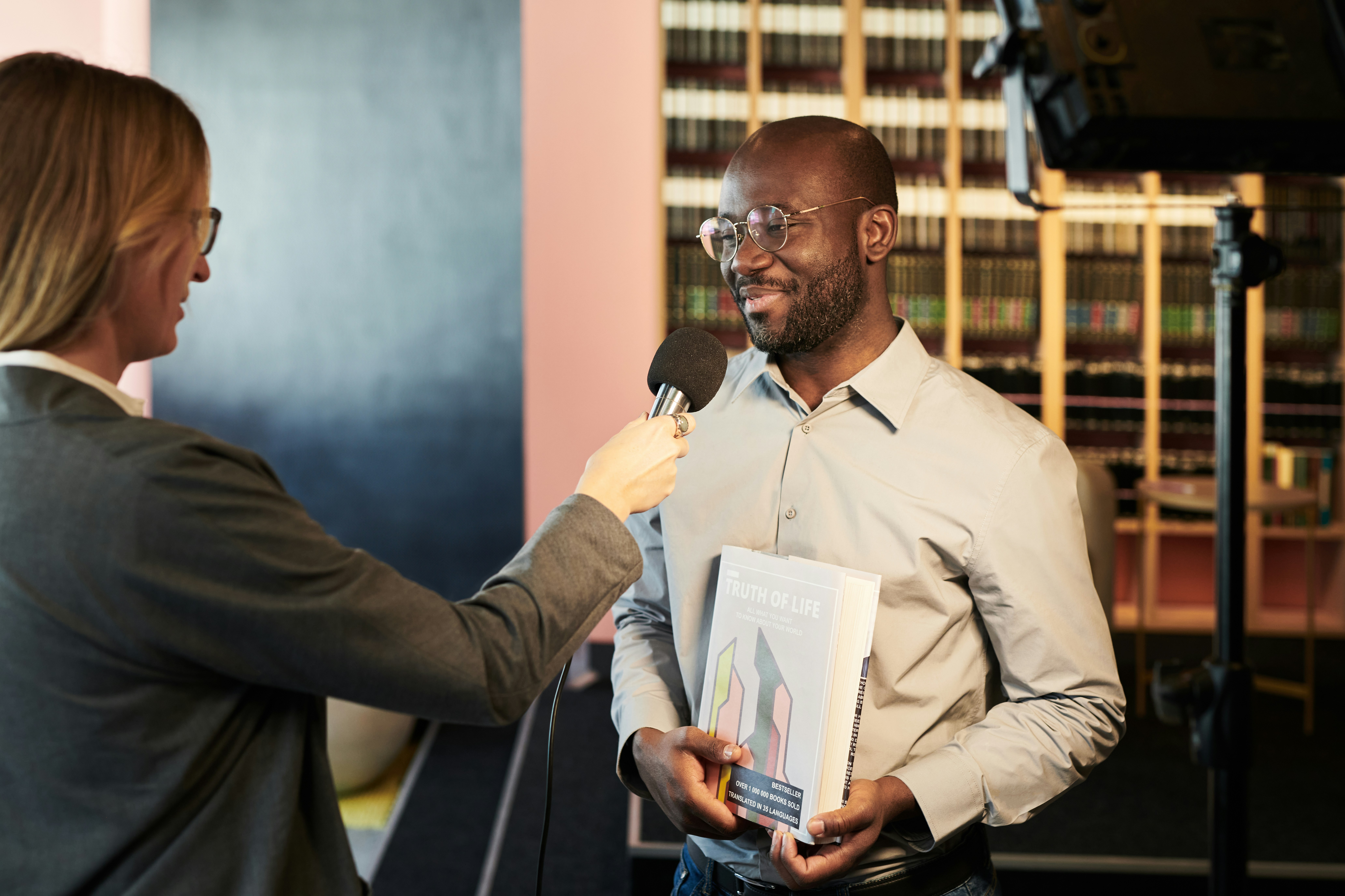 A reporter interviews a smiling man holding a book.