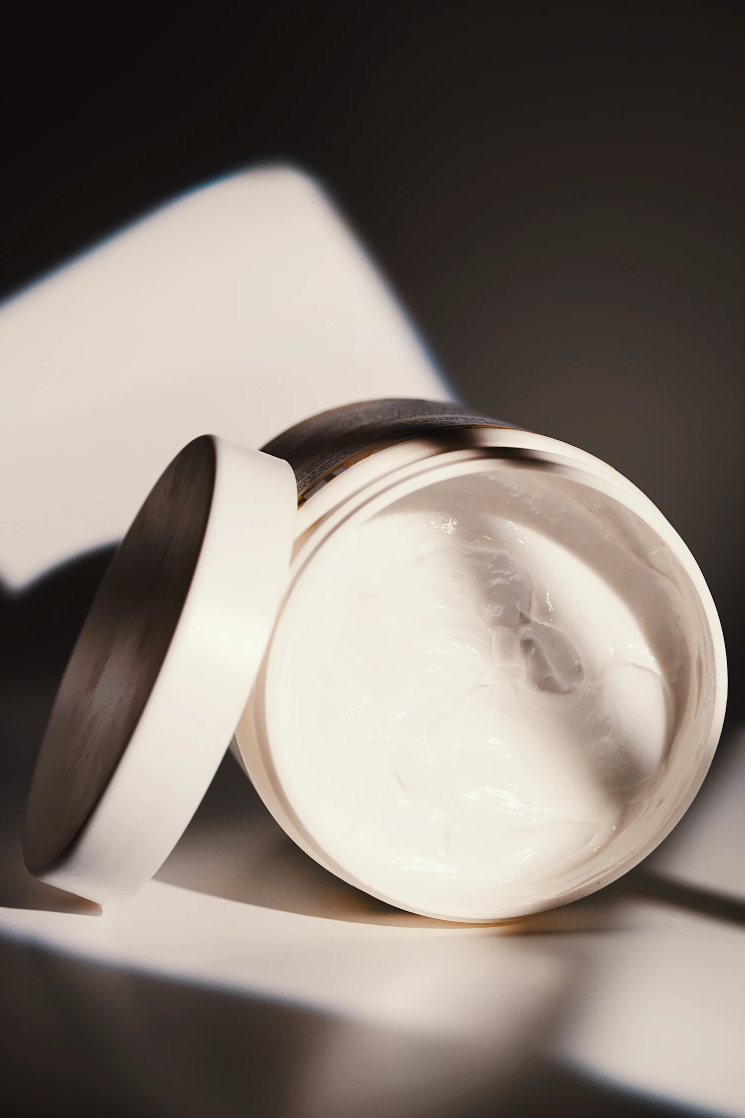 An open jar and its lid casting a hard-edged shadow on a white surface