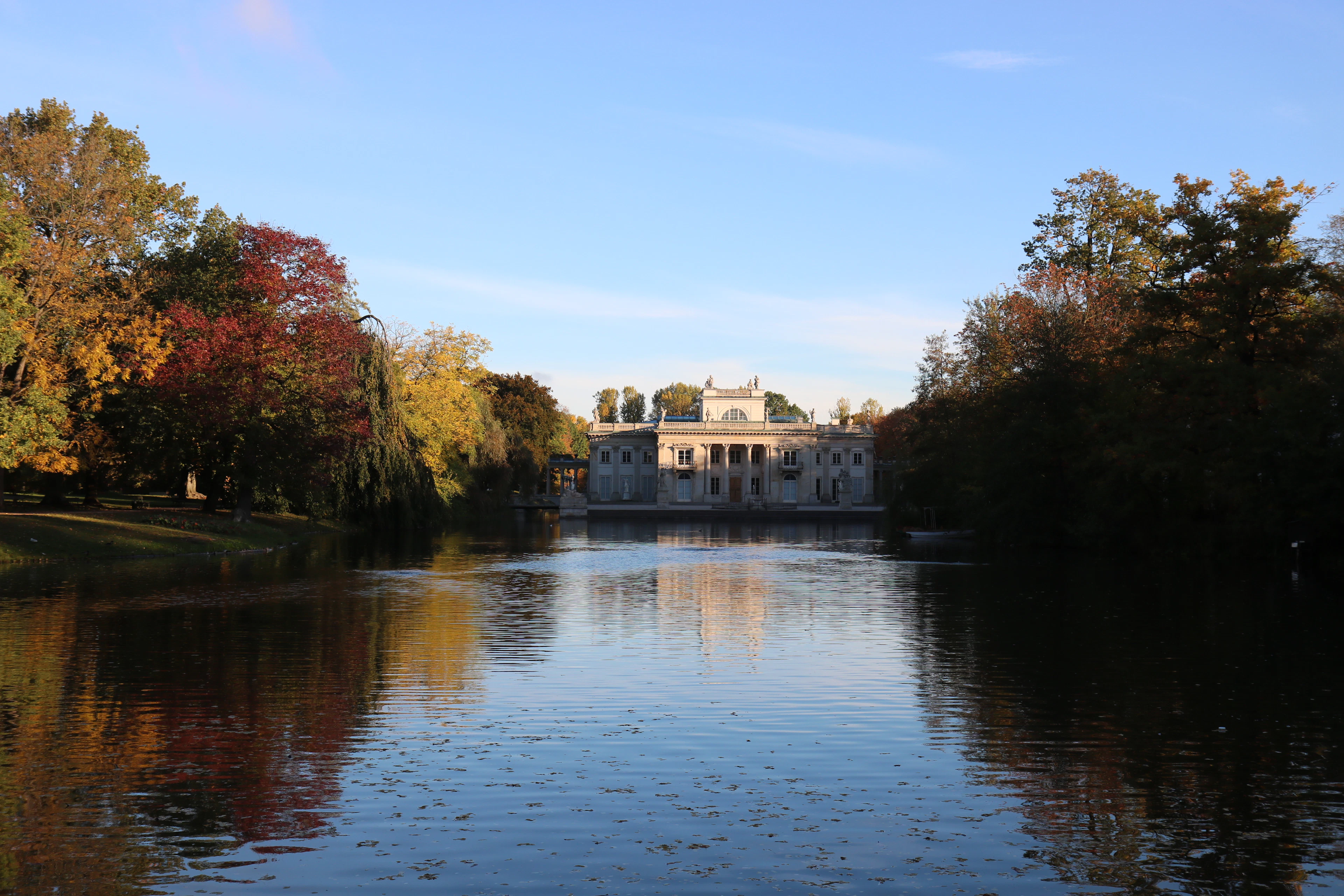 The Palace on the Water reflected in the lake at Lazienki Park, framed by autumn foliage