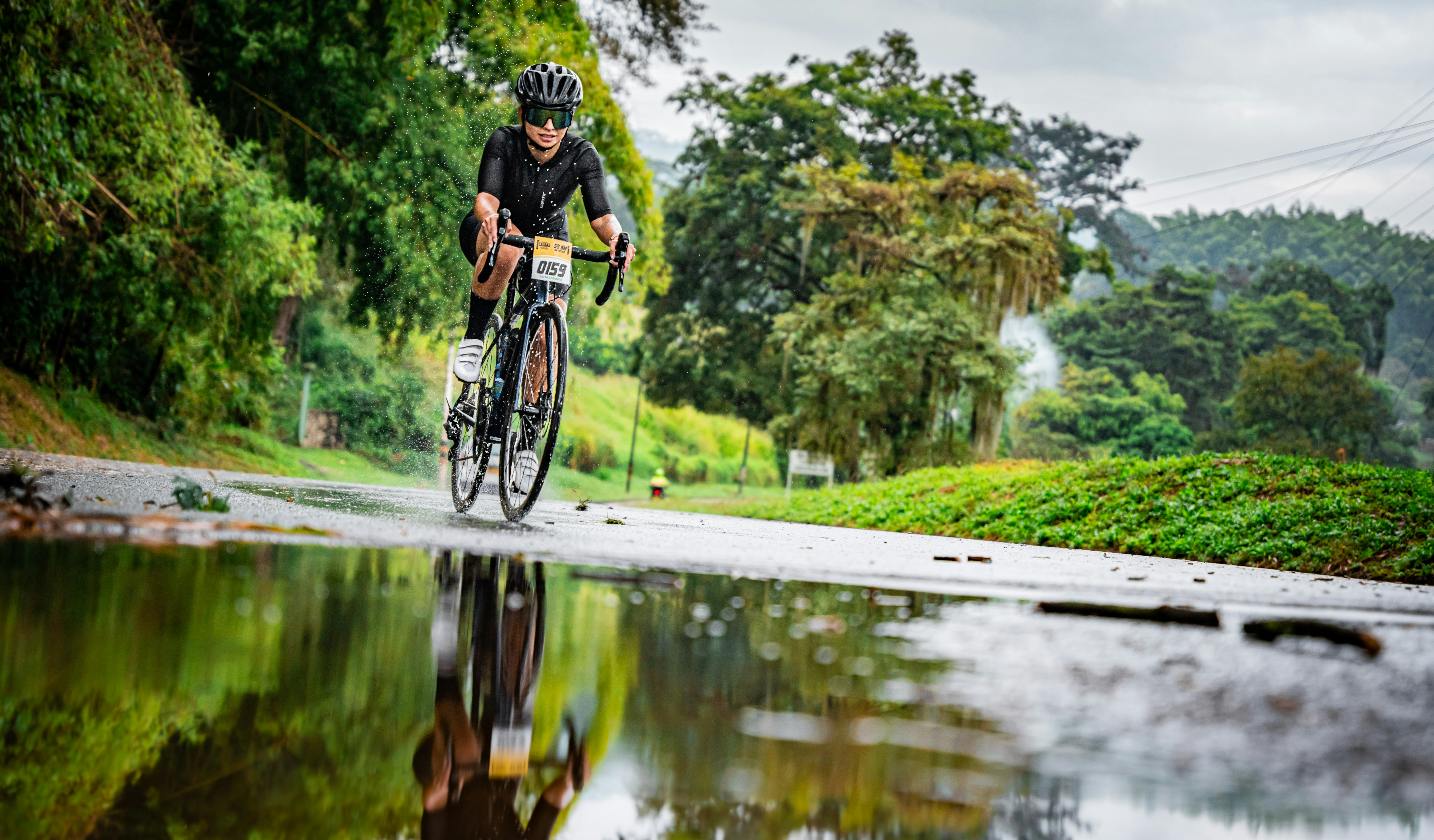 A cyclist rides through a puddle on a road.