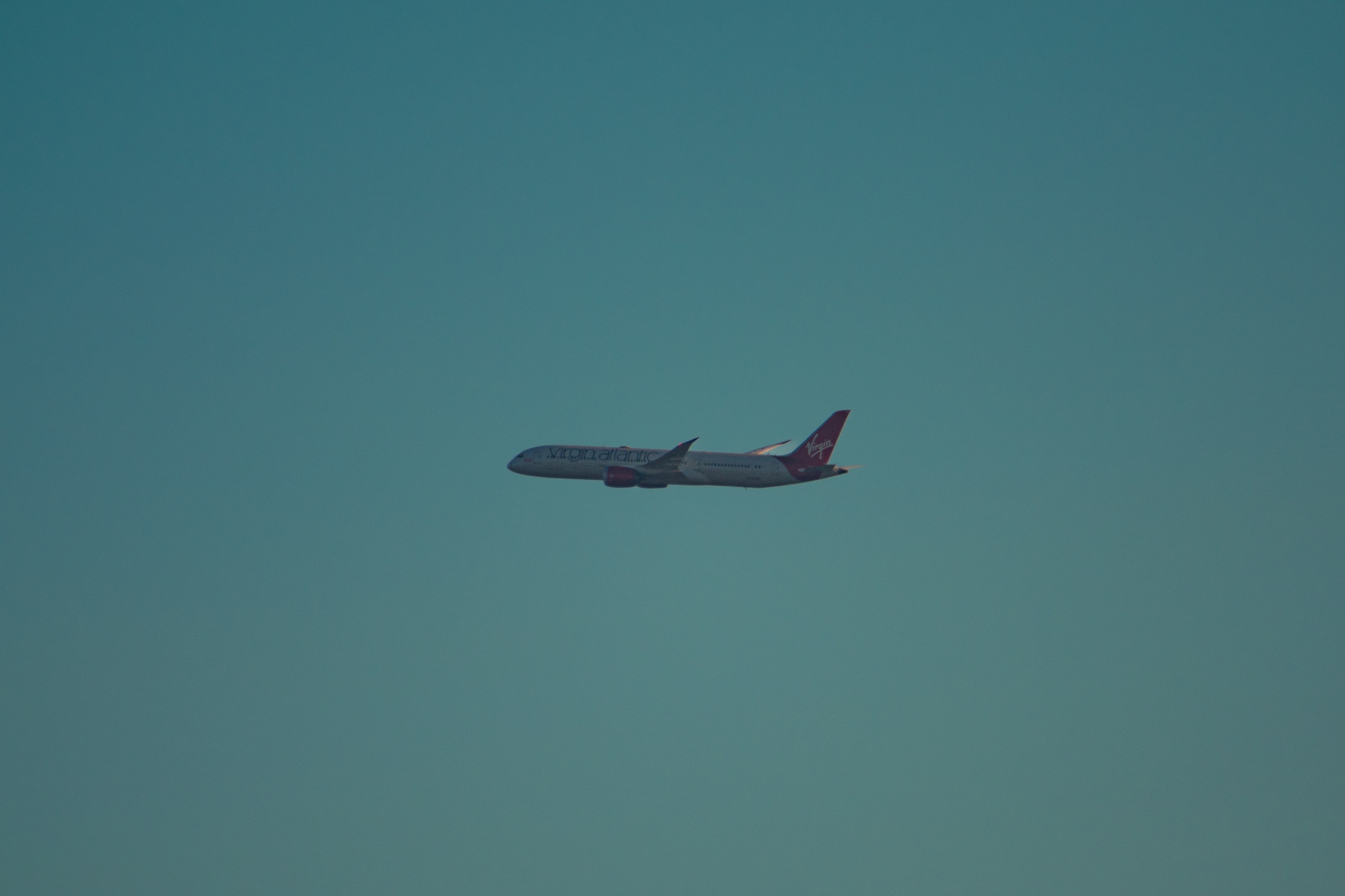 An airplane flies high in the clear blue sky.